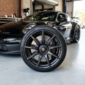 Carbon ceramic brake and wheel with Porsche logo in front of black Porsche car